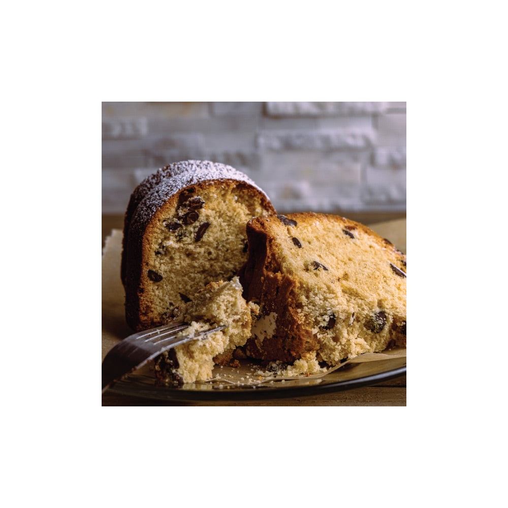 A slice of moist, fluffy coffee cake with chocolate chips and a dusting of powdered sugar on top, placed on a plate with a fork.